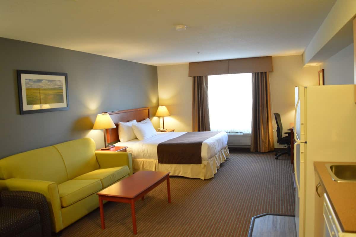 A hotel room with a bed, a yellow sofa, a small table, a desk, and a window with curtains.