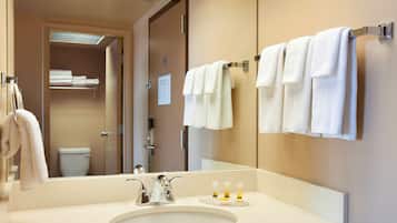 Et badeværelse på et hotel med et stort spejl, en vask og flere håndklæder hængende på en holder.