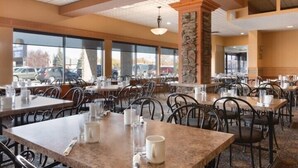 A spacious indoor dining area with multiple tables and chairs, large windows, and a stone pillar. - Border Inn and Suites Lloydminster (Lloydminster)