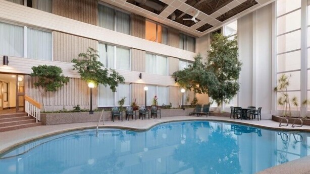 An indoor swimming pool with multiple levels, surrounded by seating areas and potted plants. - Border Inn and Suites Lloydminster (Lloydminster)