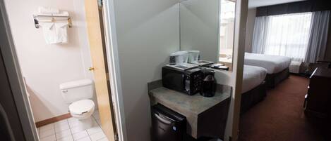 A hotel room with a toilet, a small sink with a microwave, a coffee maker, and a bed.