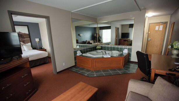 A hotel room with a bed, a desk, a chair, a TV, a bathroom with a bathtub, and a large mirror. - Super 8 by Wyndham Whitecourt (Whitecourt)