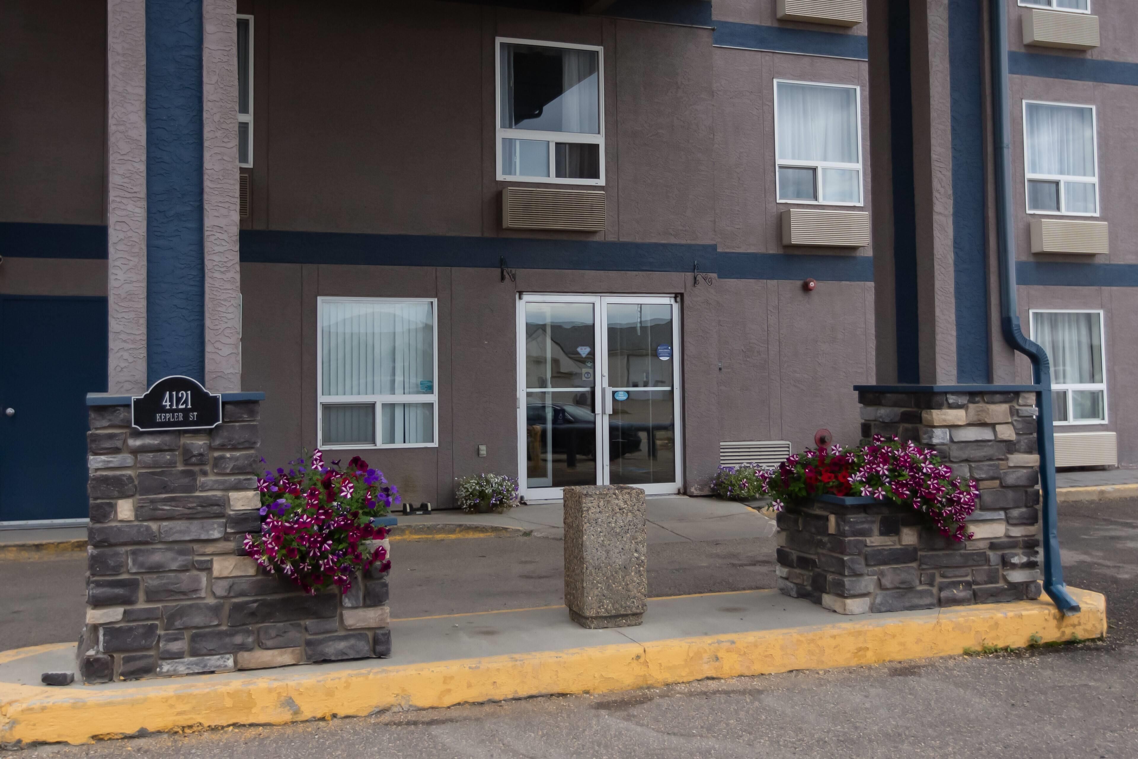 Un edificio de varios pisos con fachada de piedra, un gran acceso con puertas de vidrio y un hidrante en la acera.