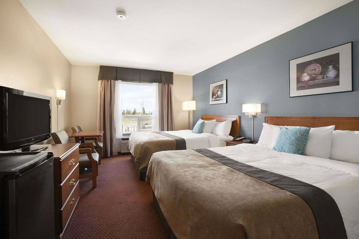A hotel room with two beds, a TV, a desk, and a window with curtains.