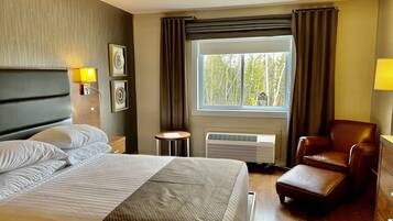 A hotel room with a bed, a chair, a small table, and a window with curtains.