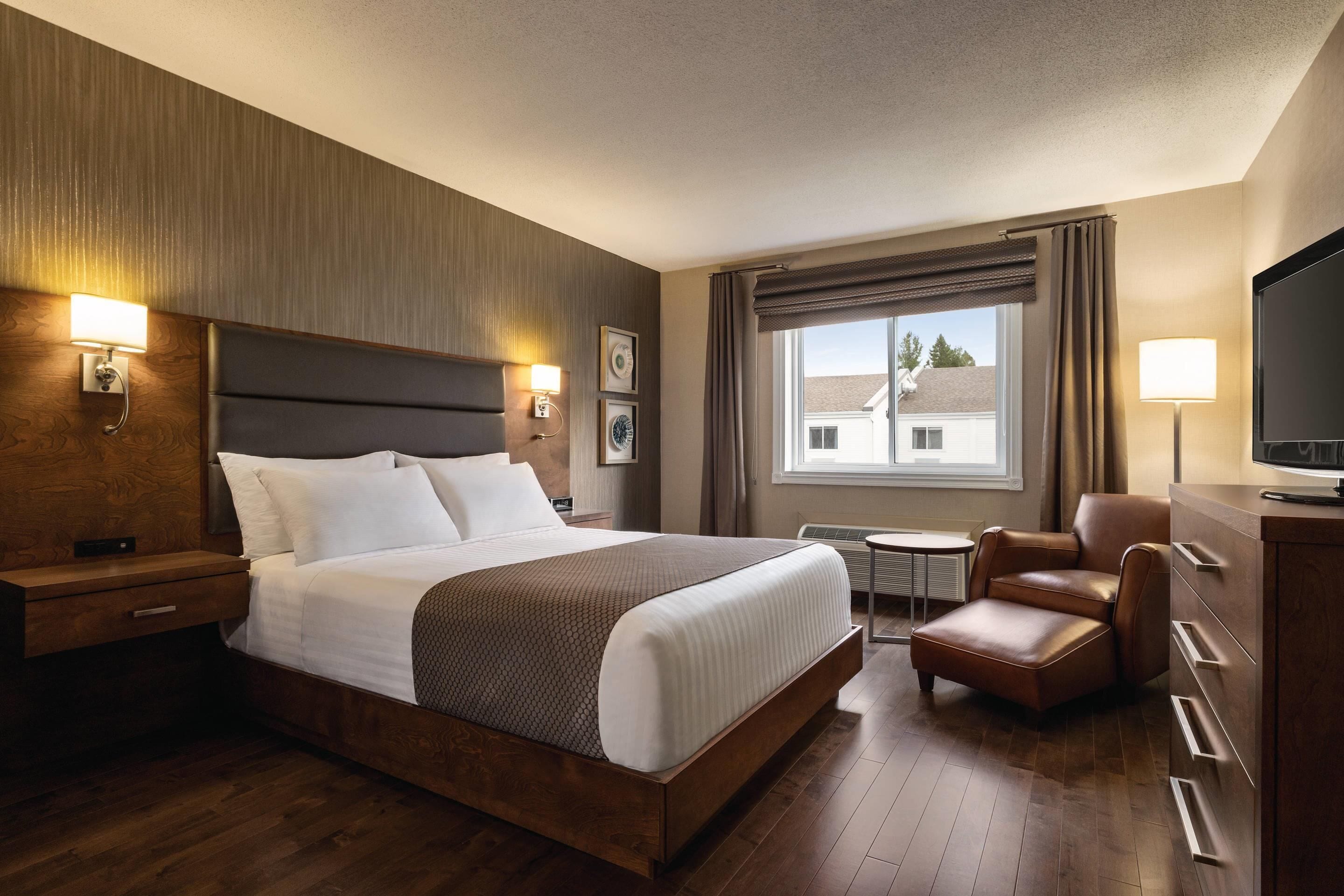 Habitación de hotel con una cama grande, una silla, un televisor y una mesita.