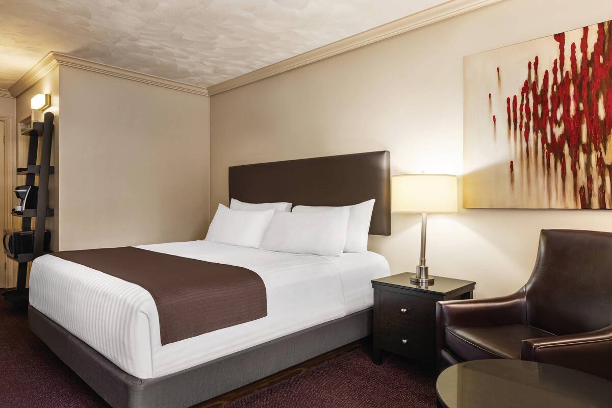 A hotel room with a large bed, a desk, a chair, a lamp, and a painting on the wall.