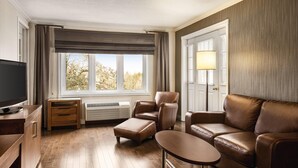 A living room with a flat-screen TV, leather sofa, ottoman, and a small table. - Atlantic Host Hotel, an Ascend Collection Hotel (Bathurst)