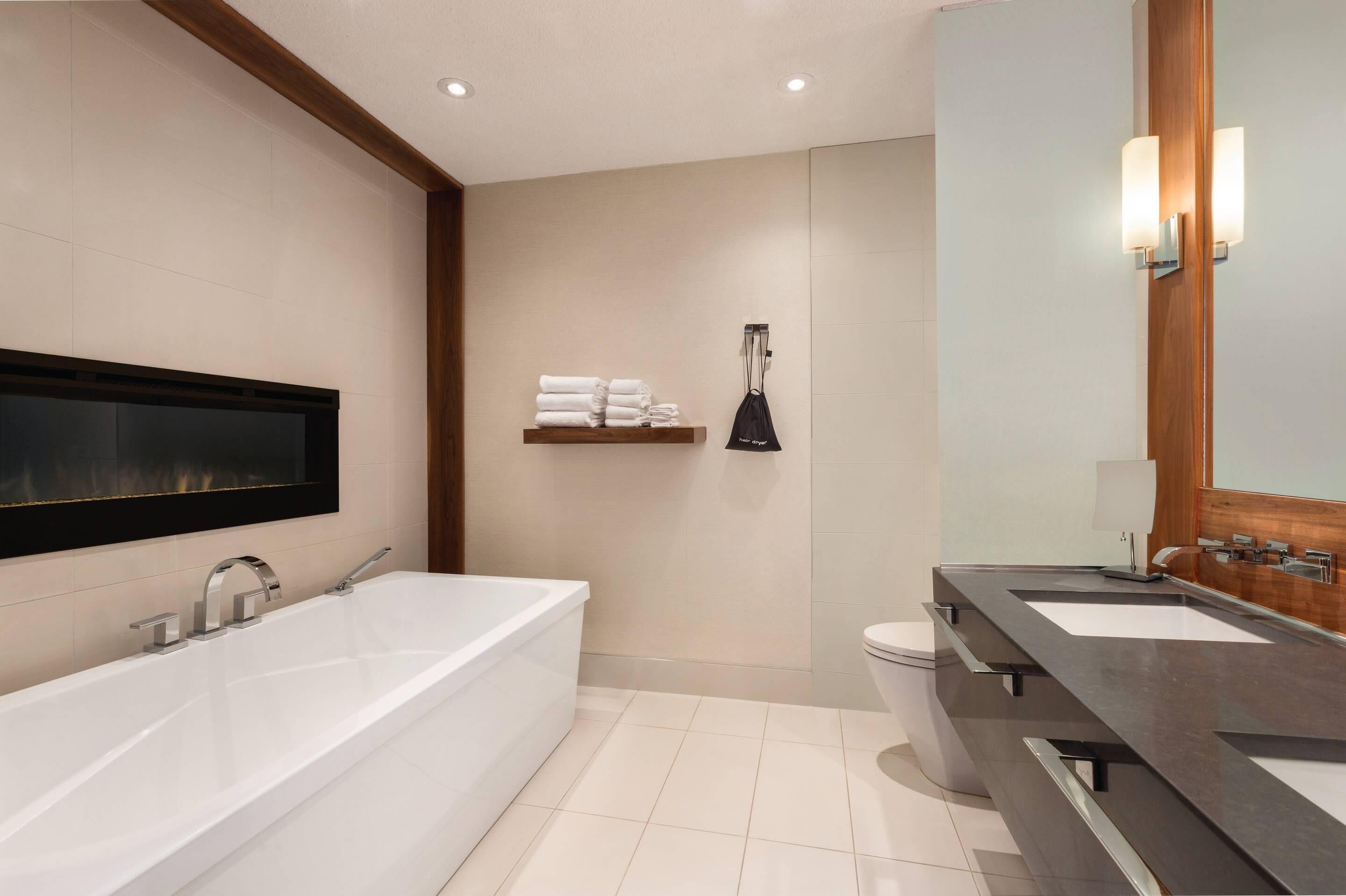 Un baño moderno con una bañera grande, dos lavamanos, un inodoro y un estante con toallas.