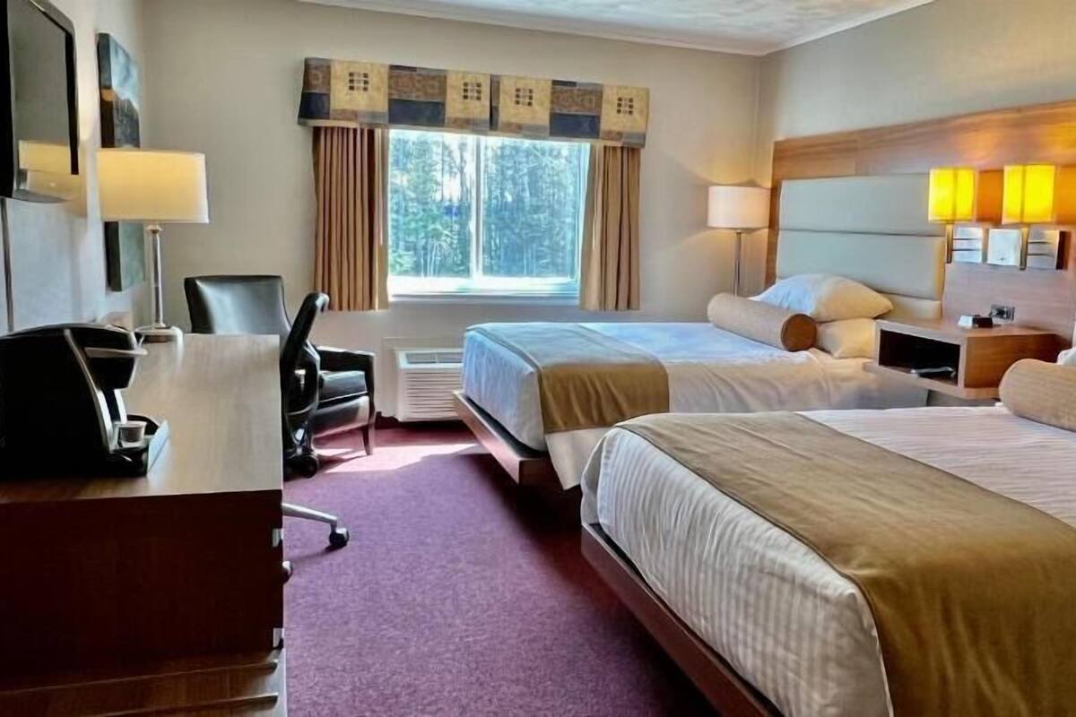 A hotel room with two beds, a desk, a chair, a coffee machine, and a window with curtains.