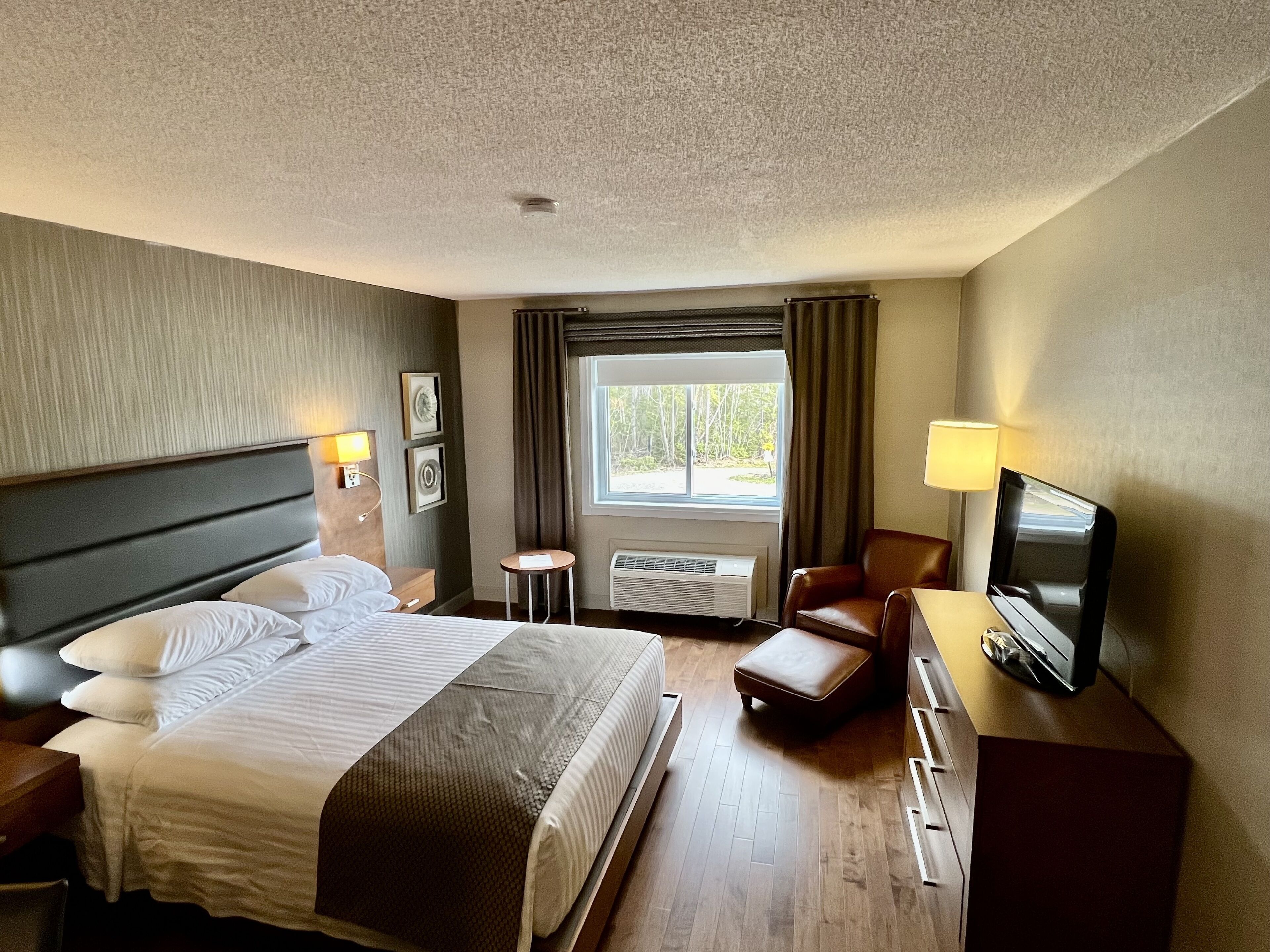 Une chambre d’hôtel équipée d’un lit, d’un bureau, d’une chaise, d’une télévision et d’une fenêtre avec des rideaux.
