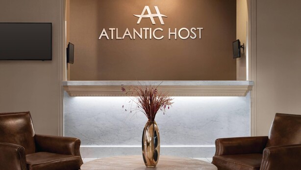 A lobby with a round table, two leather chairs, a gold vase with dried plants, and a wall with 'ATLANTIC HOST' signage. - Atlantic Host Hotel, an Ascend Collection Hotel (Bathurst)