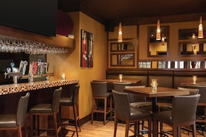 Zona de bar con mostrador, varios taburetes y vasos colgando. Hay mesas y sillas dispuestas para comer.