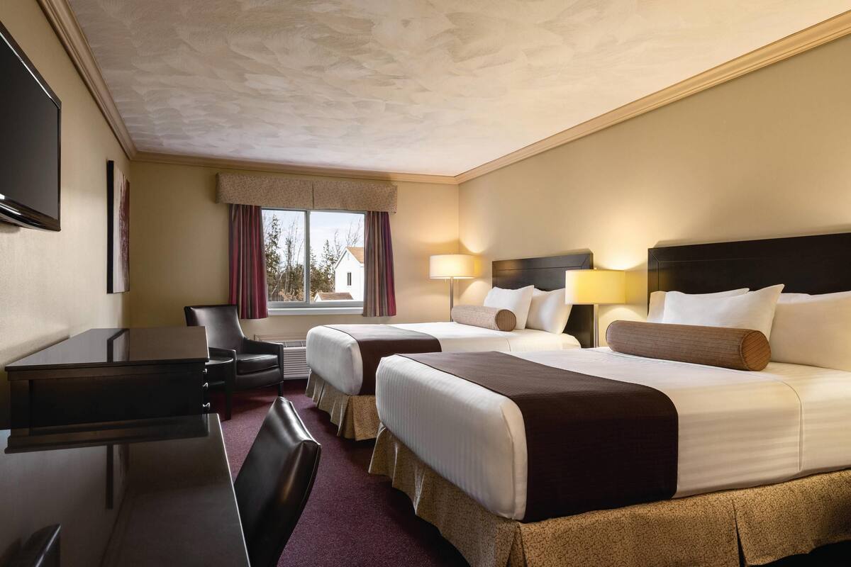 A hotel room with two beds, a desk, a chair, a TV, and a window with curtains.
