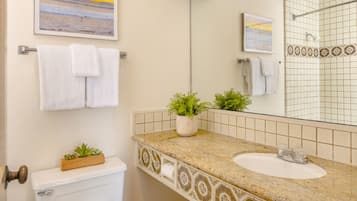 Une salle de bain avec des toilettes, un lavabo et un grand miroir. Deux plantes en pot sont posées sur le comptoir du lavabo.