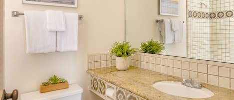 A bathroom with a toilet, sink, and a large mirror. There are two potted plants on the sink counter.