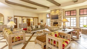 A spacious living area with a stone fireplace, wooden furniture, and large windows. - Clocktower Inn Ventura (Ventura)
