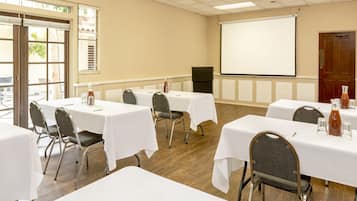 Une salle de conférence avec des tables et des chaises blanches, un écran de projection et un plancher en bois.