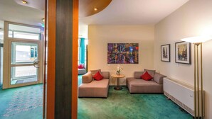 A hotel lobby with a green carpet, two sofas with red cushions, a small round table with a vase, and a painting on the wall. - PLAZA INN Blankenburg Ditzingen, Sure Hotel Collection (Ditzingen)