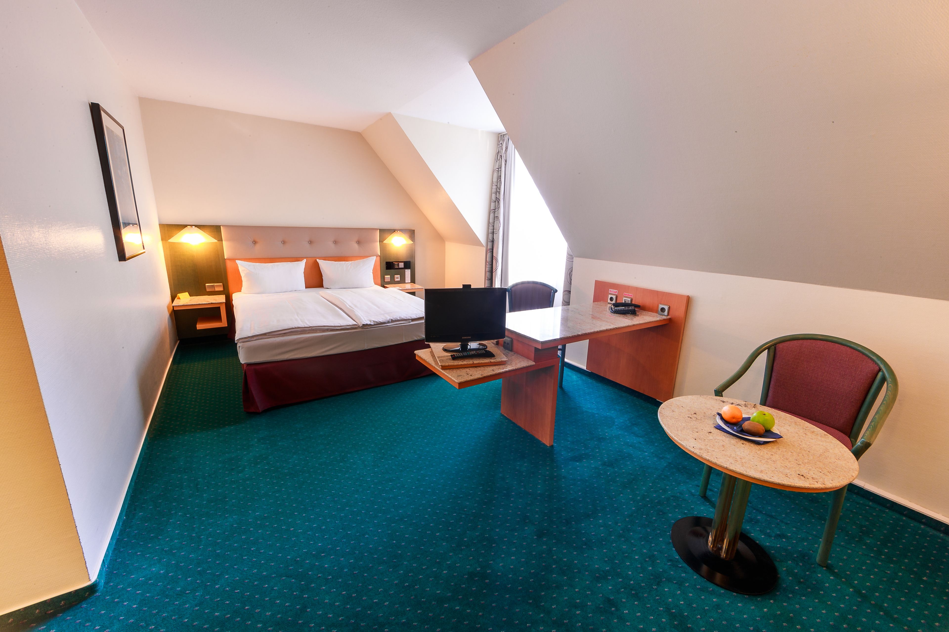 A hotel room with a bed, desk, chair, and a small table with fruit.