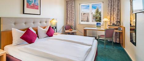Habitación de hotel con cama doble, un escritorio con silla, una mesita y un ventanal con cortinas.