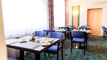 Comedor de hotel con mesas dispuestas para cuatro, sillas azules y alfombra estampada.