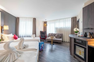 Une chambre d’hôtel avec deux lits, un canapé, une table à manger, une télévision et un minibar.