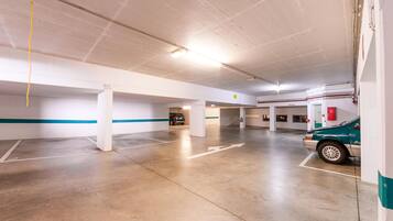 A spacious indoor parking area with concrete floors and white walls, featuring directional arrows and a fire extinguisher.
