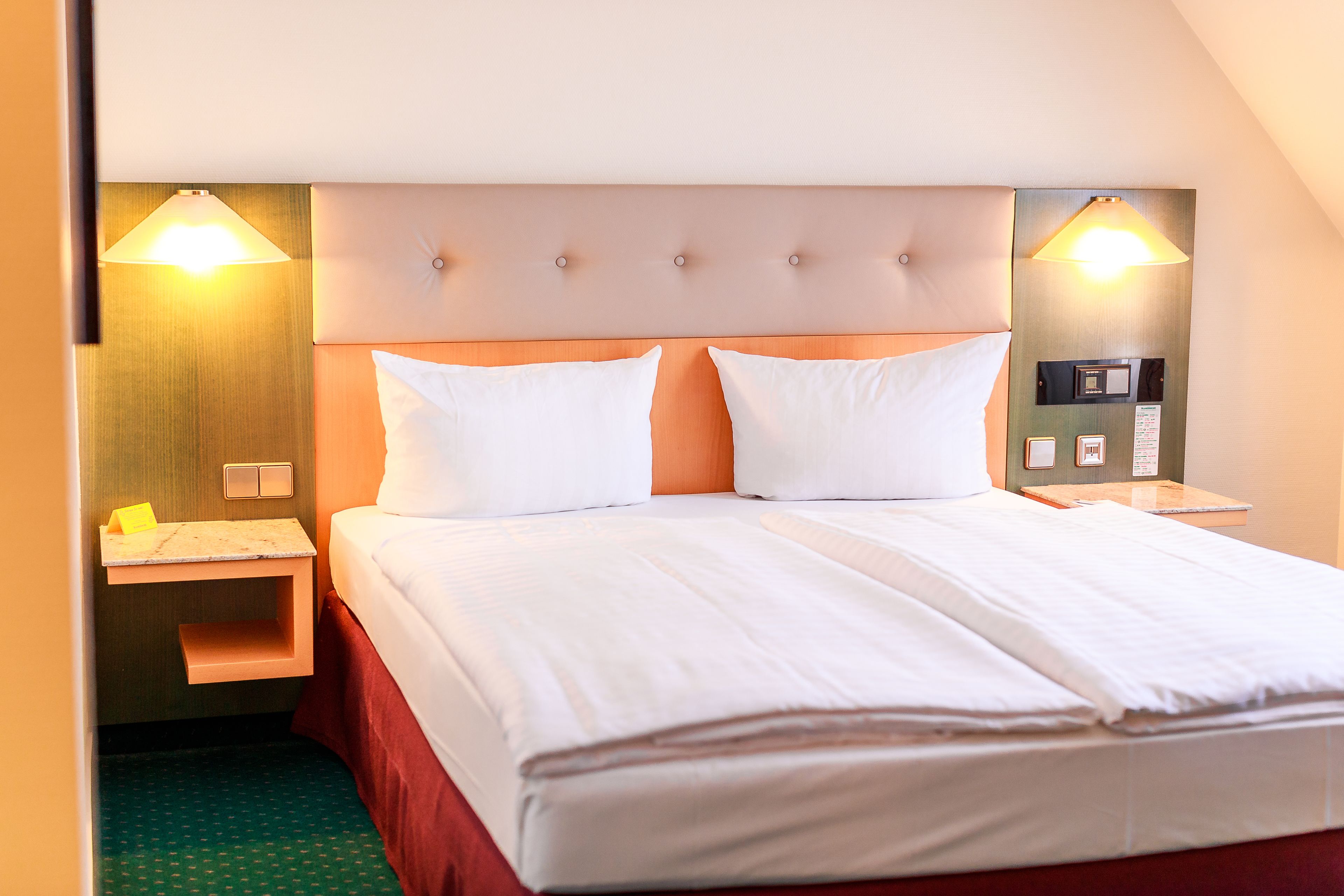A hotel room with a double bed, two bedside tables, a nightstand, and a wall-mounted lamp.