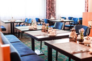 A hotel dining area with tables set for breakfast, blue upholstered chairs, and a carpeted floor. - PLAZA INN Blankenburg Ditzingen, Sure Hotel Collection (Ditzingen)