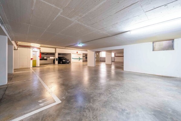 Un amplio garaje con pisos de concreto y paredes blancas, con múltiples espacios de estacionamiento y algunas columnas.