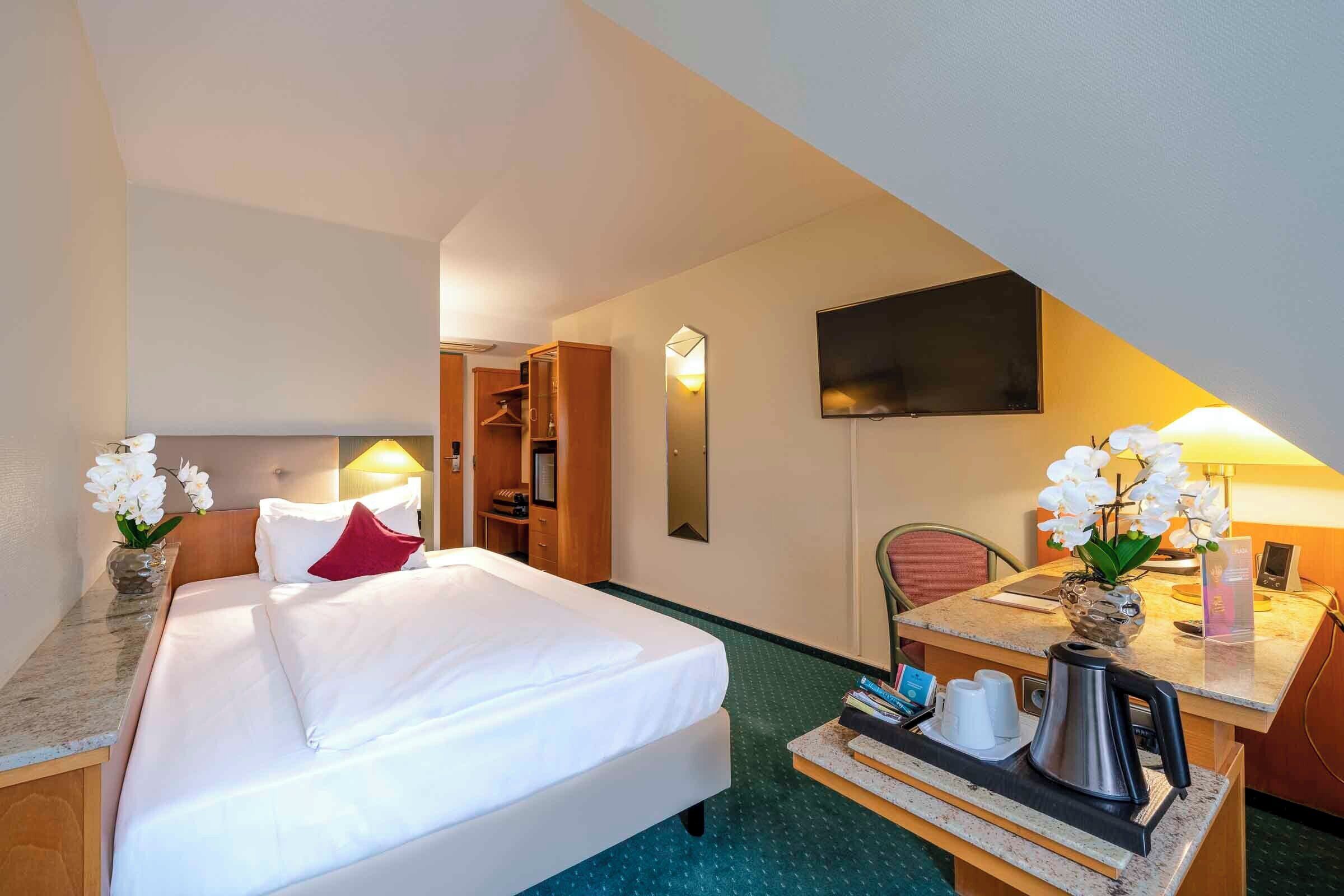 A hotel room with a bed, a desk with a coffee maker, a TV, and a bathroom with a shower.