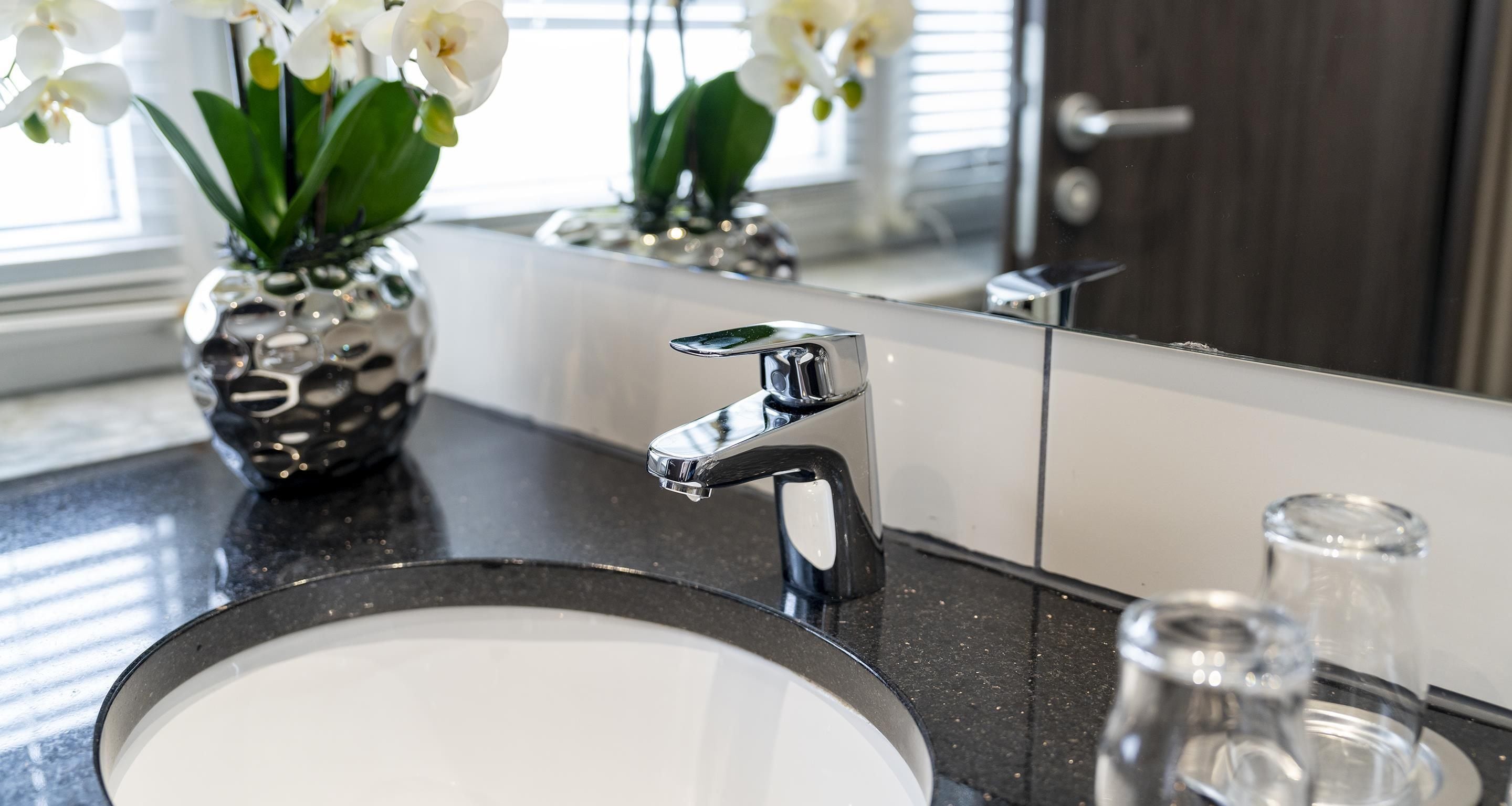Une salle de bain avec un lavabo moderne, un robinet chromé et un vase contenant des fleurs blanches.