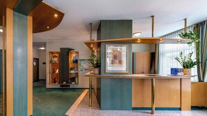 A reception area with a wooden reception desk, a framed picture, and a potted plant. - PLAZA INN Blankenburg Ditzingen, Sure Hotel Collection (Ditzingen)