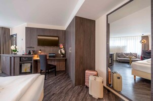A hotel room with a bed, a desk with a computer, a television, and a large mirror reflecting the room.