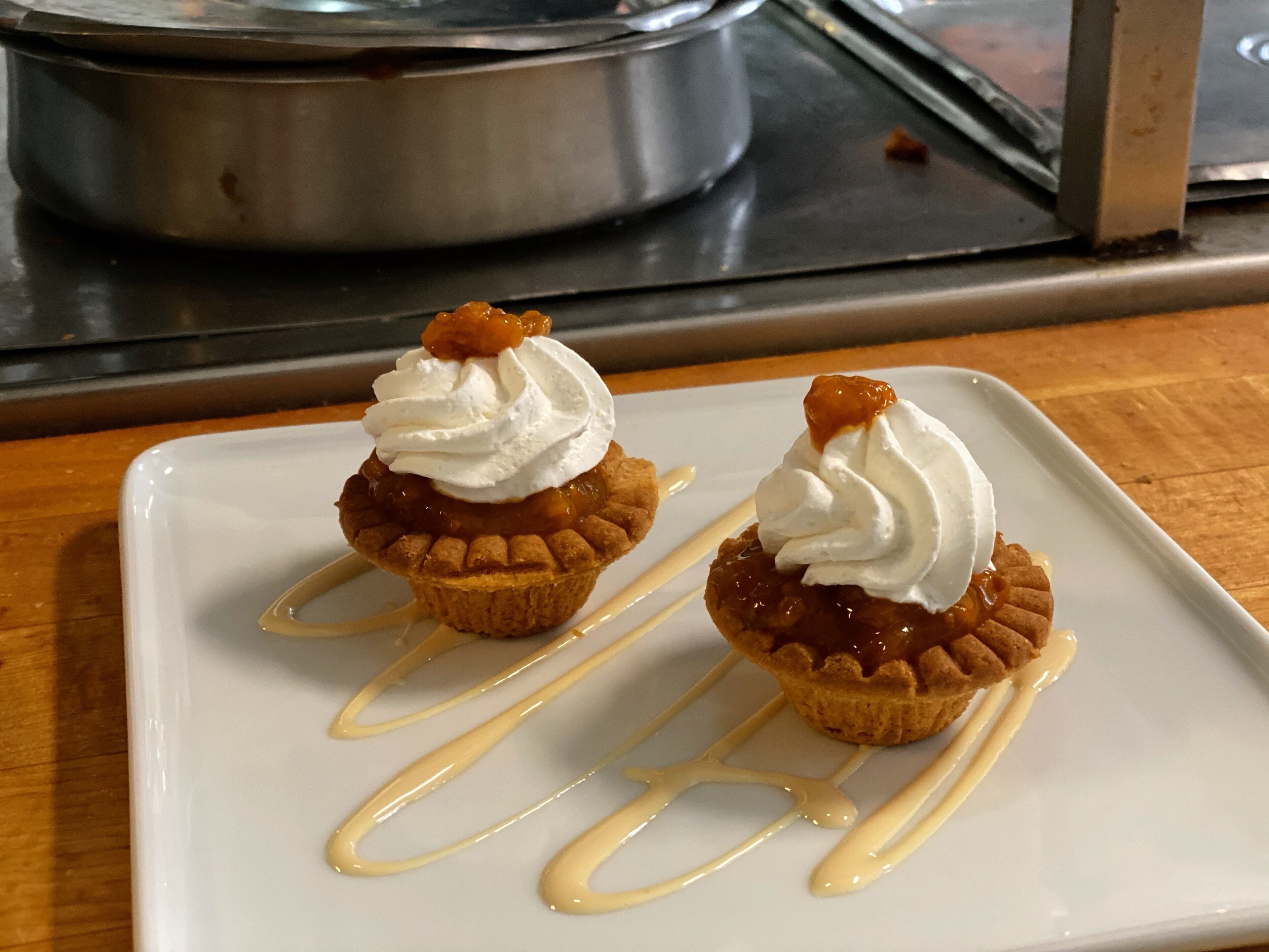 Two mini pies with whipped cream and caramel sauce on a white plate.
