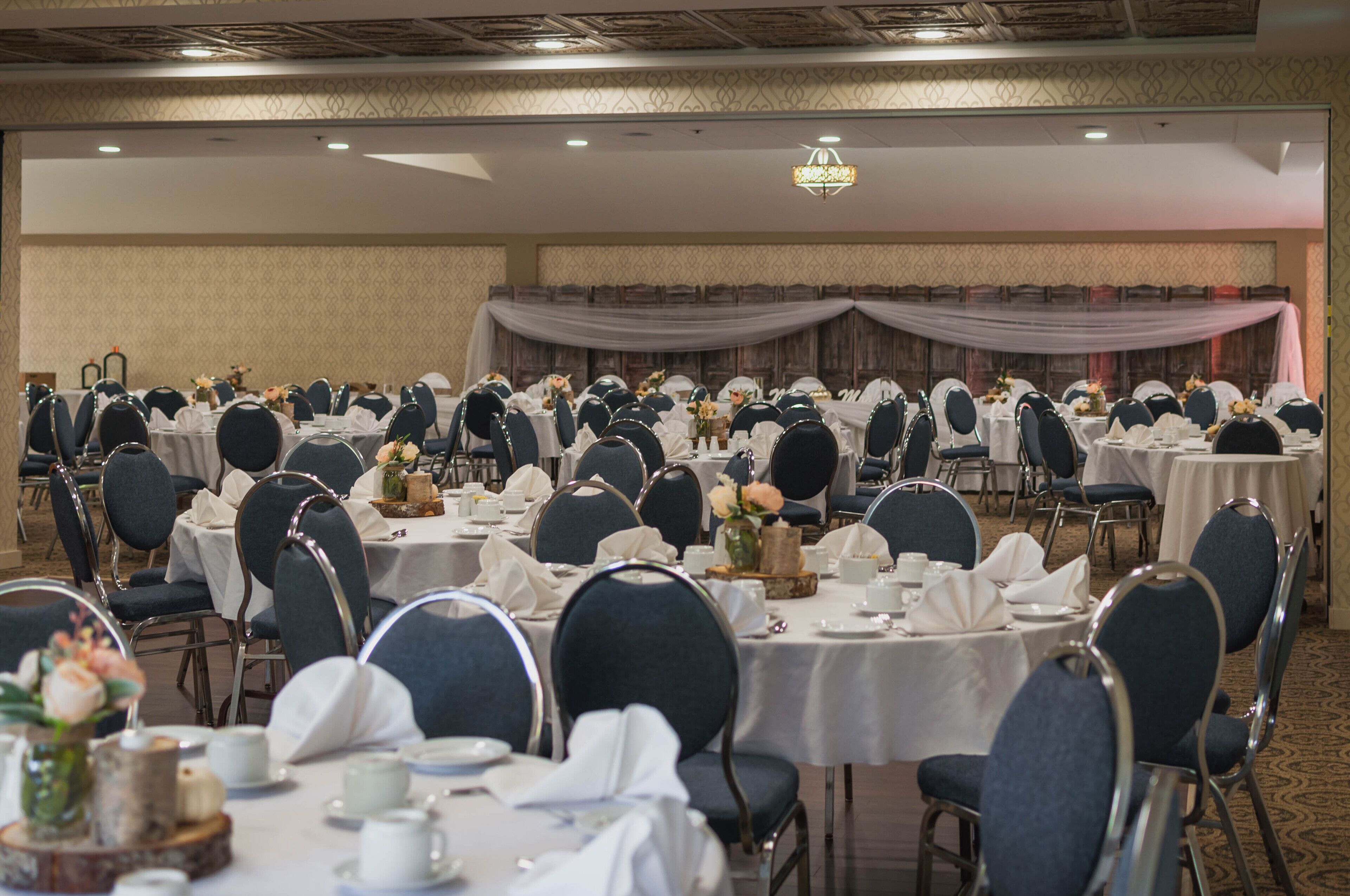 Une salle de banquet avec des tables rondes dressées pour le repas, chacune étant agrémentée de chaises et de couverts.