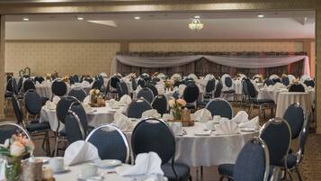 Une salle de banquet avec des tables rondes dressées pour le repas, chacune étant agrémentée de chaises et de couverts.