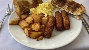 Un plato de comida para el desayuno con tostadas, huevos revueltos, salchichas y patatas asadas.