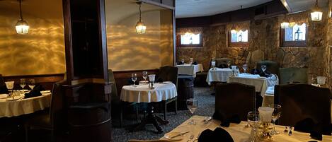A restaurant with multiple tables, stone walls, and hanging lights.