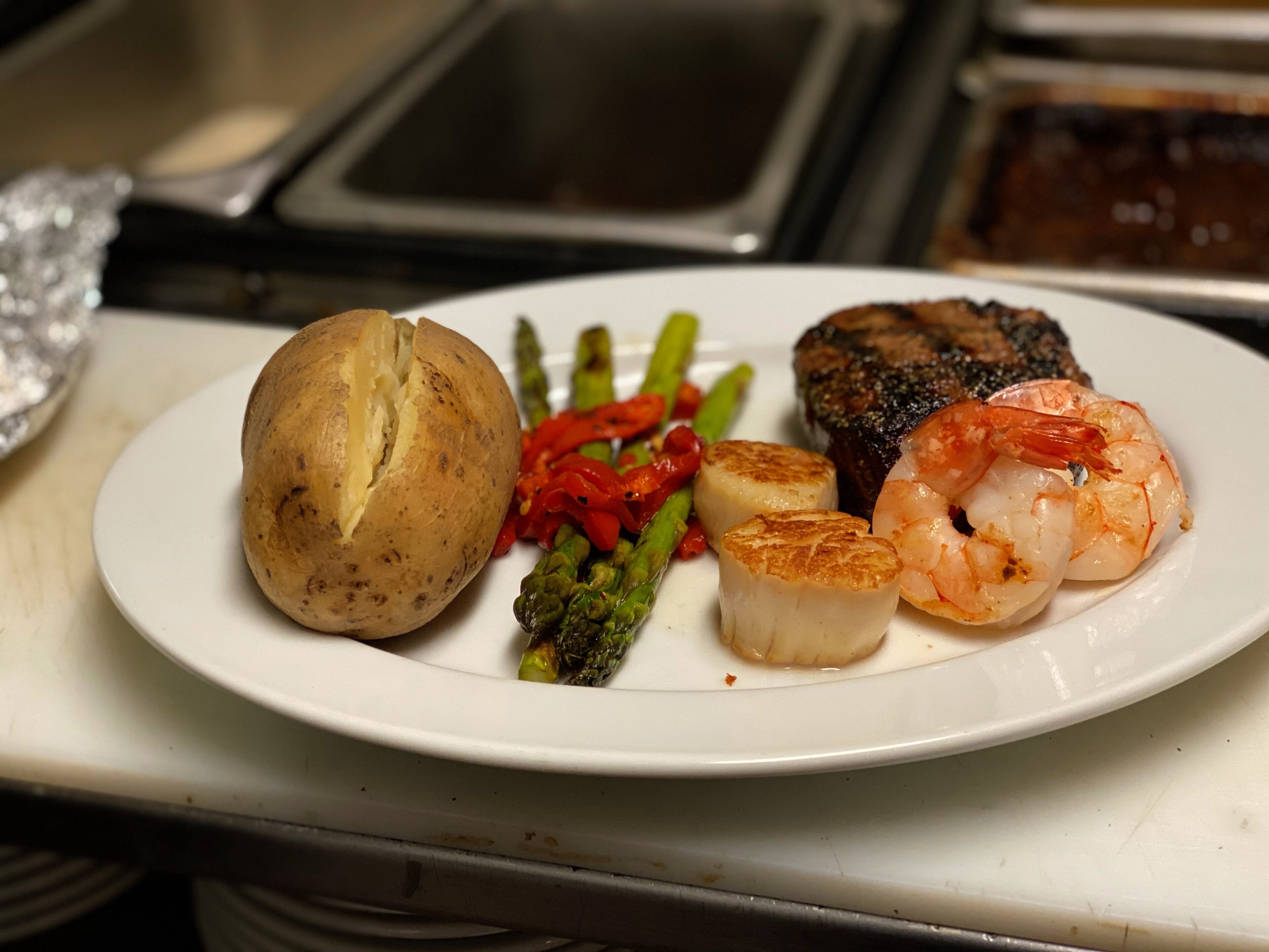 Plat de menjar amb entrecot, gambes, cloïsses, espàrrecs i patata.