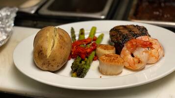 Plat de menjar amb entrecot, gambes, cloïsses, espàrrecs i patata.