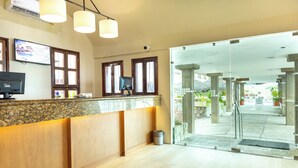 A reception area with a wooden counter, two monitors, and a glass door leading outside. - Hotel Sands Arenas (Mazatlán)