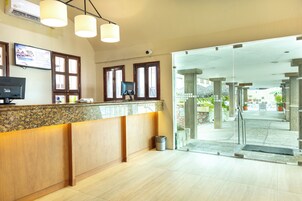 Zona de recepción con mostrador de madera, dos monitores y una puerta de vidrio que da al exterior.