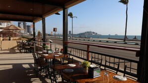 A restaurant with outdoor seating overlooking a beach and cityscape. - Hotel Sands Arenas (Mazatlán)