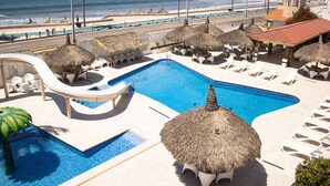 A resort pool area with a water slide, thatched umbrellas, and lounge chairs. - Hotel Sands Arenas (Mazatlán)