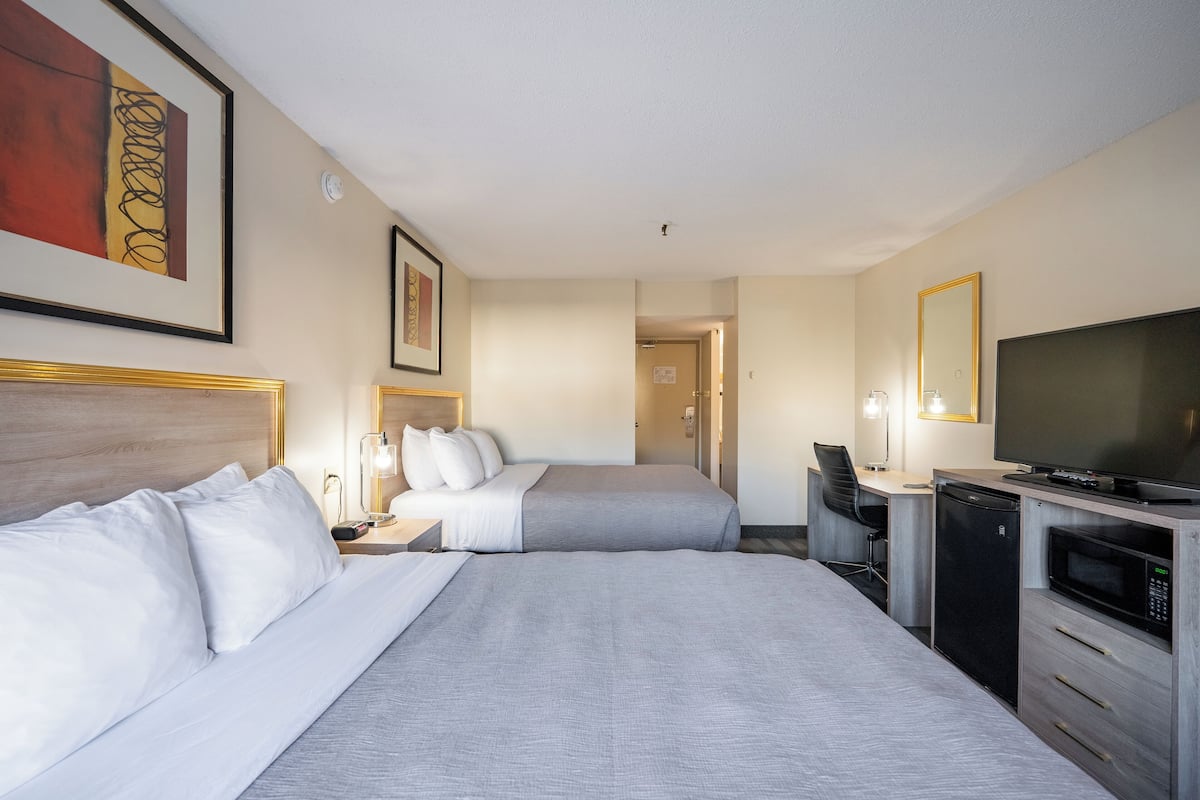 A hotel room with two beds, a desk, a television, and a microwave.