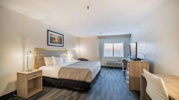 Ein Hotelzimmer mit Bett, Nachttisch, Lampe, Schreibtisch, Stuhl, Fernseher und einem Fenster mit Vorhängen.