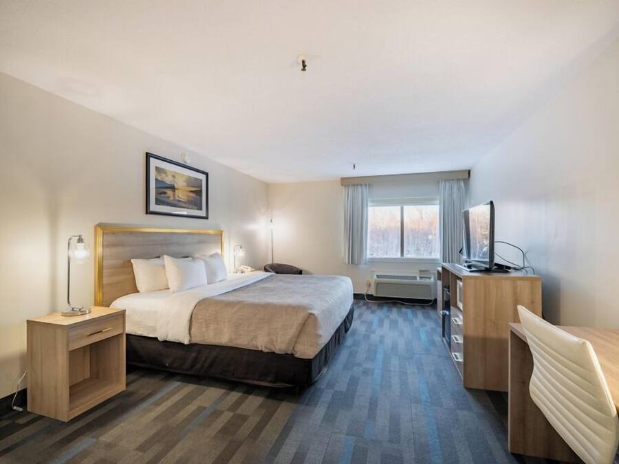 A hotel room with a bed, bedside table, lamp, desk, chair, TV, and a window with curtains.