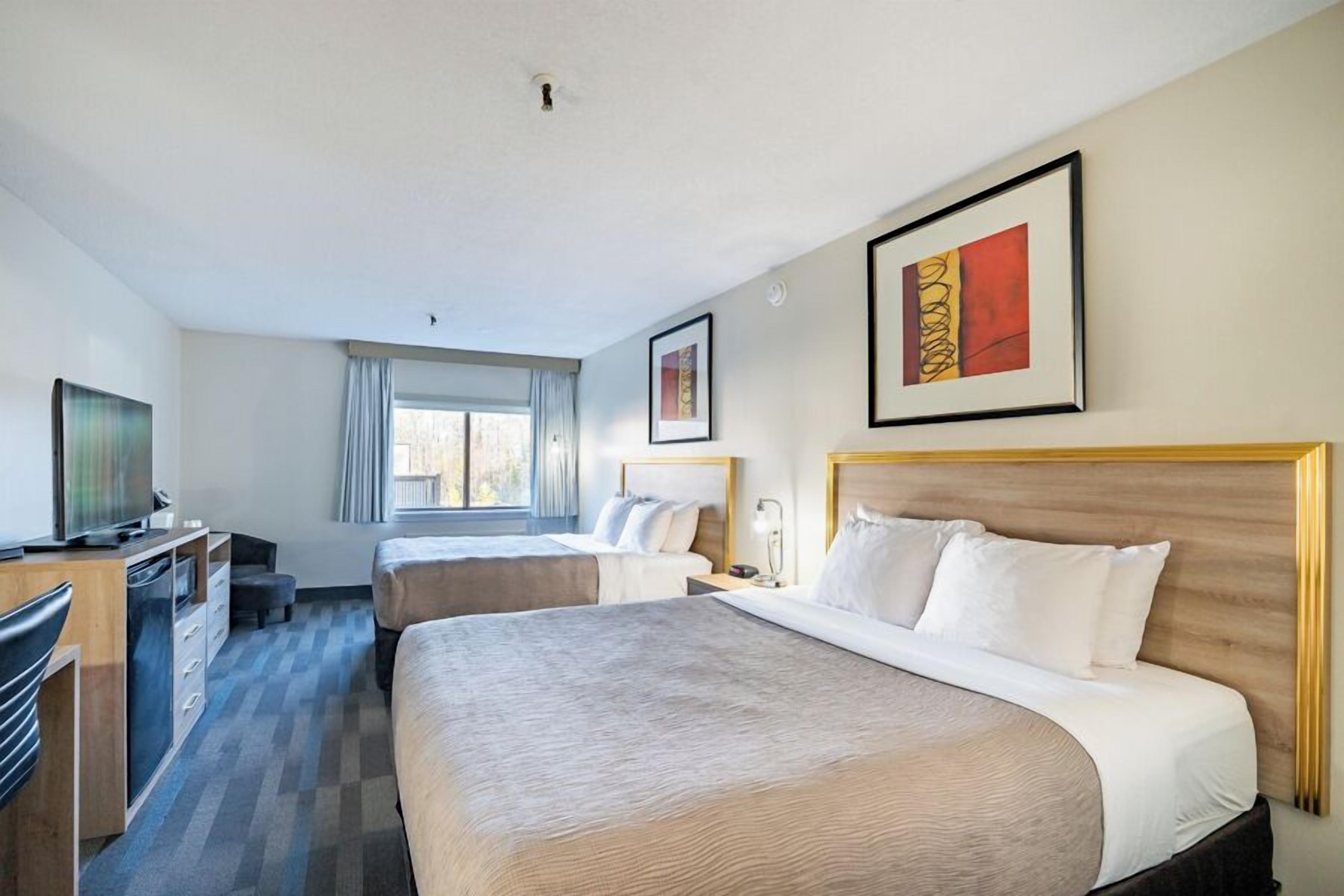 Quarto de hotel com duas camas, uma escrivaninha, televisão e obras de arte nas paredes.